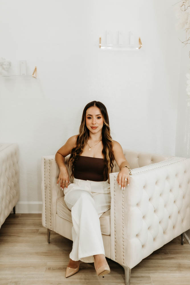 Carol Hoyos sitting confidently in a cream tufted chair, looking directly at the camera